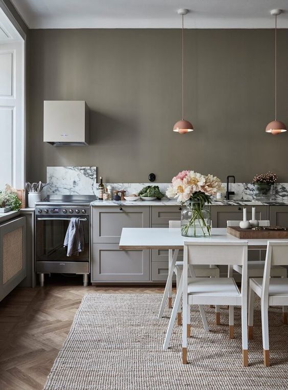 https://www.digsdigs.com/photos/2023/04/a-chic-olive-green-kitchen-with-grey-cabinets-a-small-hood-pink-pendant-lamps-a-white-dining-table-and-chairs.jpg
