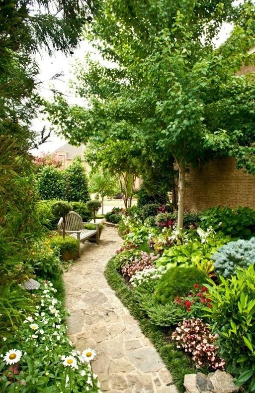 a gorgeous blooming side yard with lots of greenery and various flowers, a tree and a wooden bench feels like a secret garden