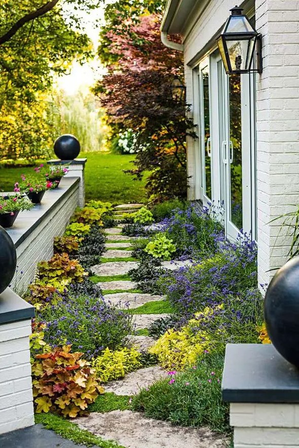 a floral side yard with an irregular stone path, bright blooms and greenery, potted plants and blooms around