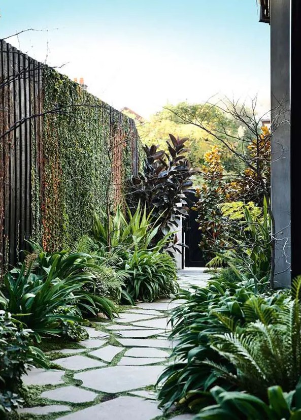 a beautiful and dreamy side yard with an irregular stone path with greenery, lots of lush greenery around and twigs is cool