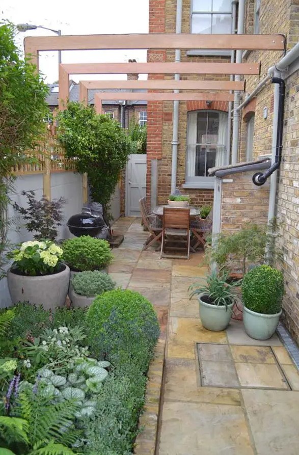 a small yet welcoming side yard with a stone deck, greenery and blooms, a folding wooden dining set and a grill