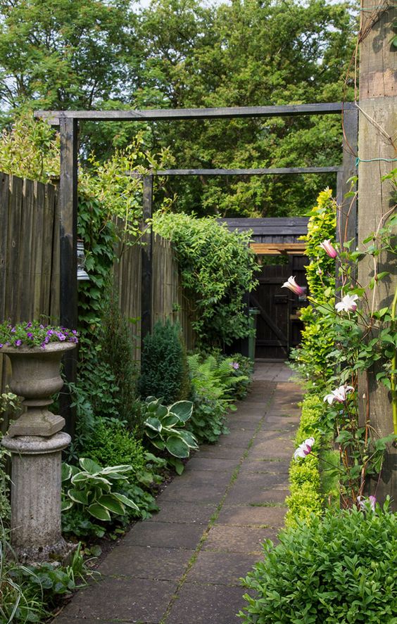 a refined vintage-inspired side yard with a pavement path, greenery and blooms, climbing plants and a vintage urn with blooms