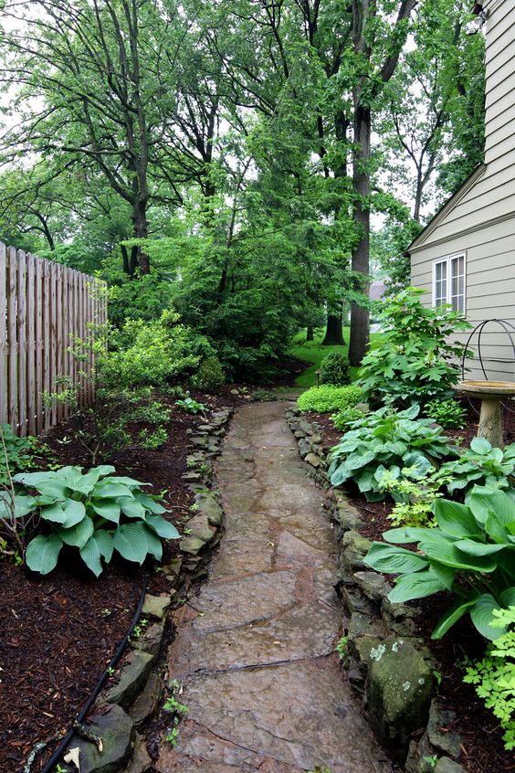 a simple shadowy side yard with greenery and an irregular stone path plus a bird bath is welcoming