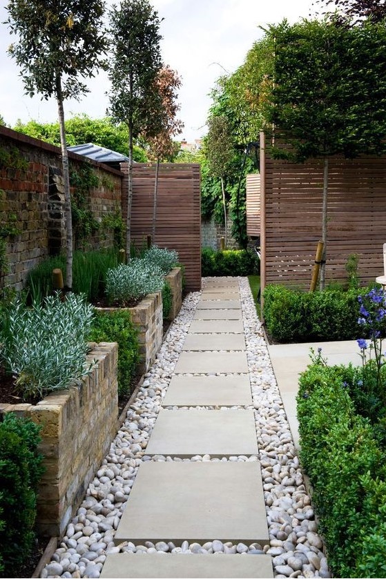 a welcoming pathway with large brick flower beds with greenery and pebbles on the ground with large tiles