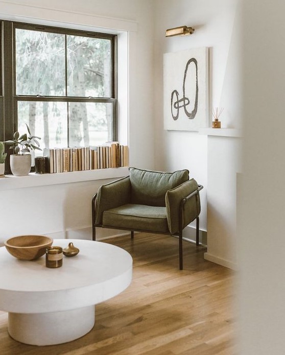 a beautiful sitting nook with an olive green chair that echoes the frames, some books, artwork and a fireplace