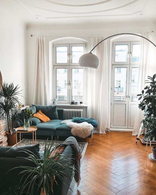 a cool Scandinavian living room with green sofas, potted plants, book stacks, a bold rug, a gloor lamp and some pillows