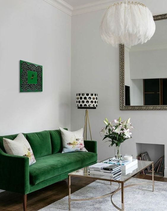 a formal living room with a faux fireplace with books, a green sofa, a floor lamp with a whimsy lampshade, a pendant lamp and a glass coffee table