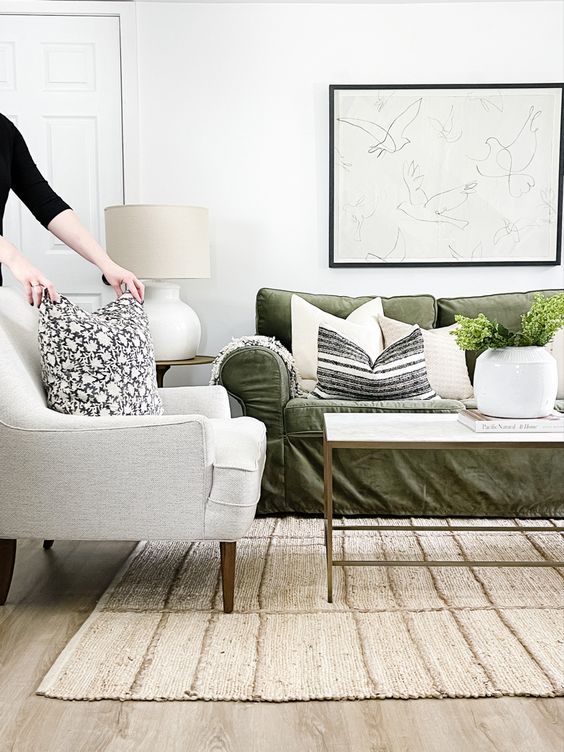 a lovely living room with a green sofa, a neutral chair, some printed pillows, a coffee table, an artwork and greenery