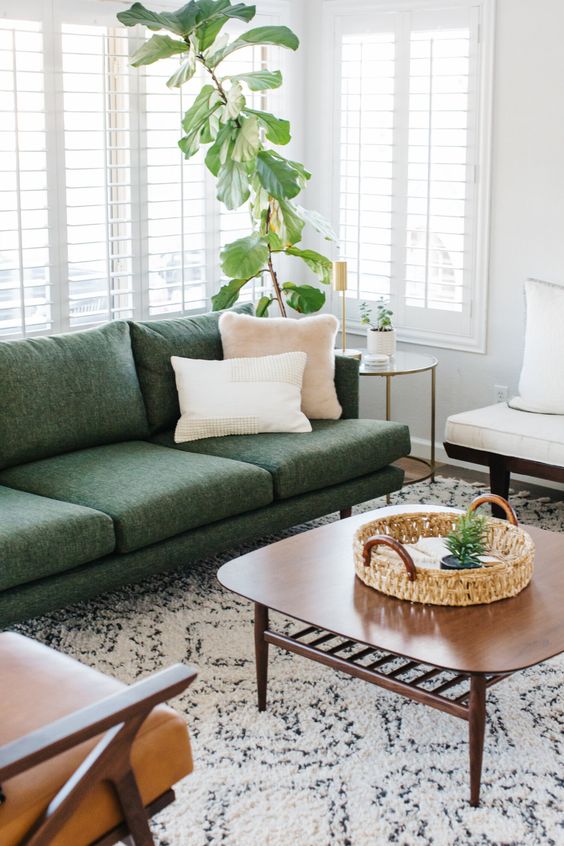 a neutral living room with a green sofa, a tan and a white chair, a coffee table and some potted greenery is welcoming