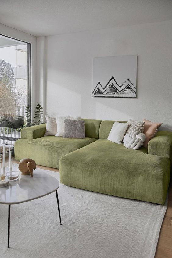 a neutral living room with a low green sofa and neutral pillows, a coffee table with some decor, a neutral rug and a fun artwork