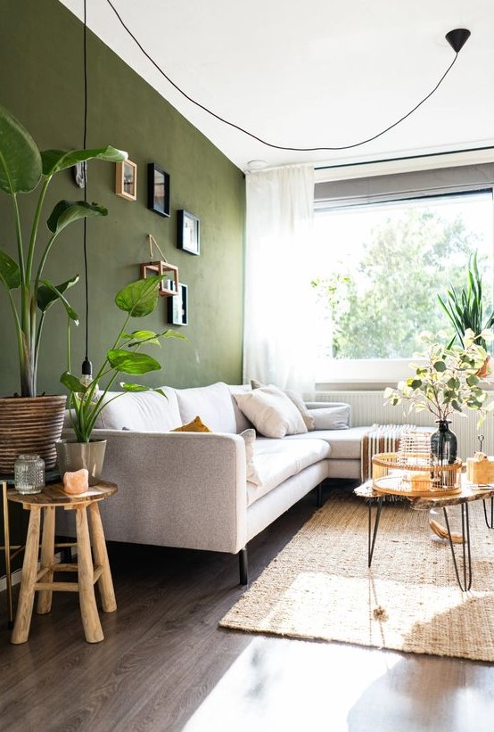 a stylish living room with an olive green accent wall, a neutral sofa, some coffee tables, a gallery wall and some plants