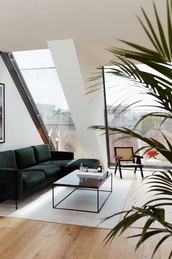 an attic space with large skylights, a dark green sectional, a coffee table, a cool cane chair and a neutral rug