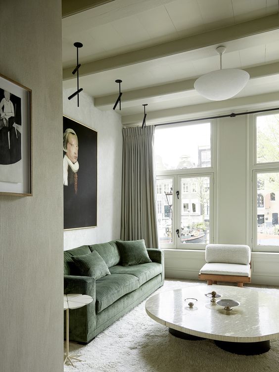 an elegant living room with some bold artwork, a green sofa, a neutral chair, a low coffee table and a side table plus some lights