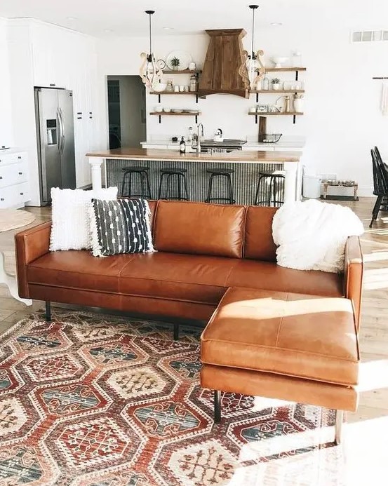 a brown leather corner sofa used as a space divider for an open layout of a kitchen and a living room