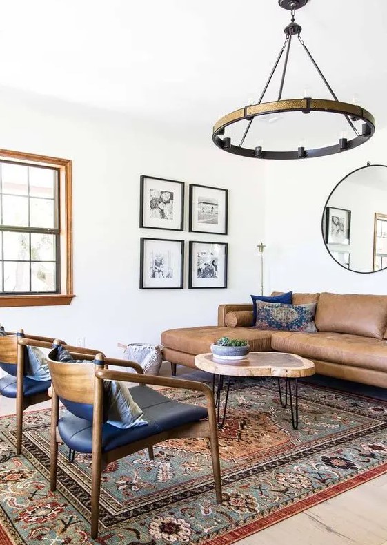 a mid-century modern living room with a brown leather sectional, a round coffee table, black chairs, a boho printed rug