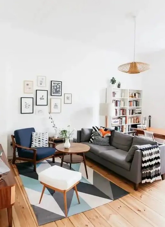 a mid-century modern living room with a bold printed rug, a grey sofa, a navy chair and a white stool, a cool gallery wall