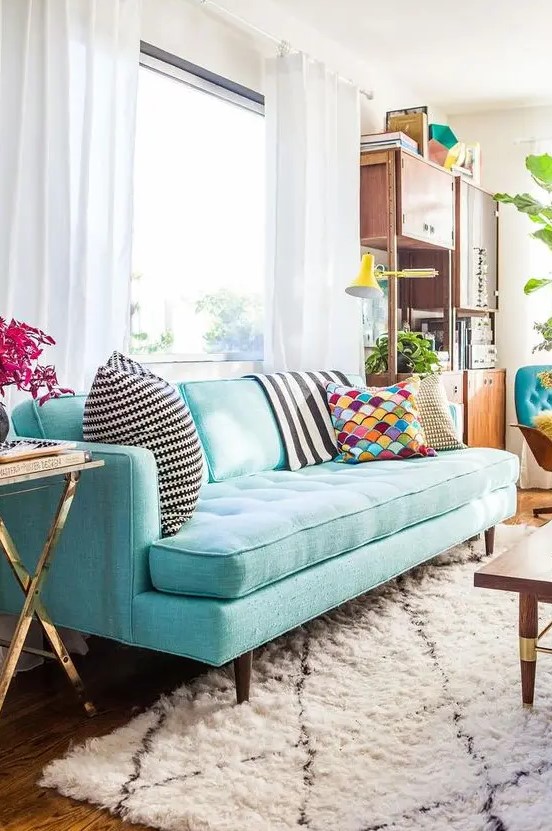 a pretty living room with a modern turquoise sofa, a modern storage unit, a coffee table and touches of gold here and there