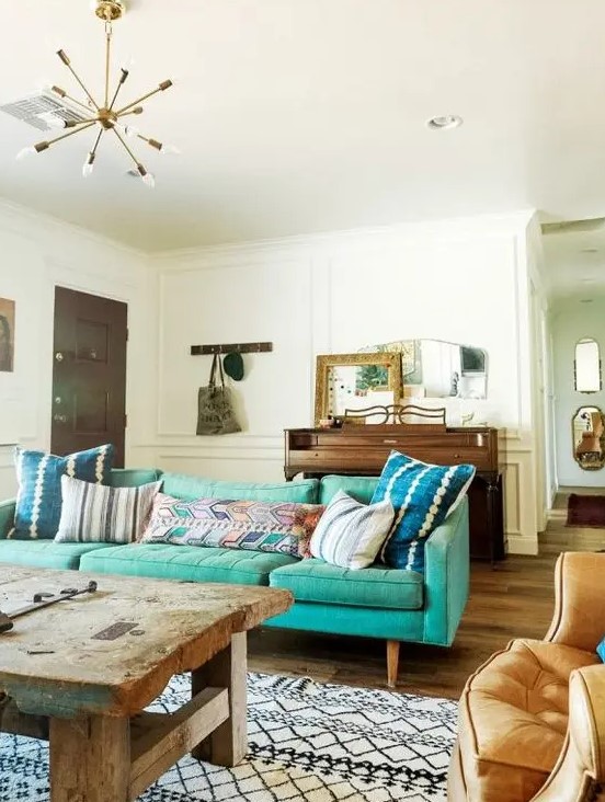 an eclectic living room with a mid-century modern turquoise sofa, a rough wooden table, a chair, a wooden dresser and some mirrors on it