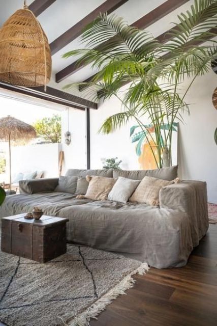 a tropical living room with a grey linen sofa and pillows, a dark-stained chest, woven lamps and a bold artwork