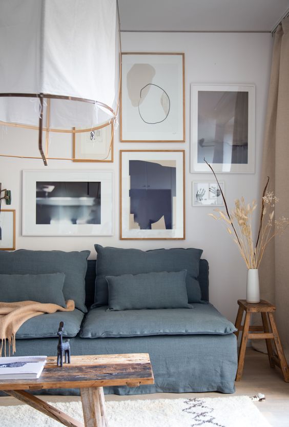 a coastal living room with a blue linen sofa, a bench with decor, an abstract gallery wall and a pendant lamp