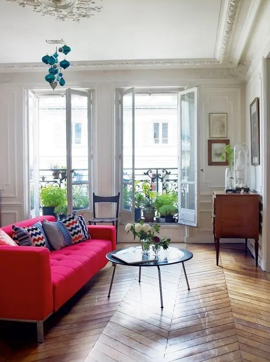 an elegant living room with a hot pink tufted sofa, a low table, a wooden sideboard and lots of potted plants in the balcony