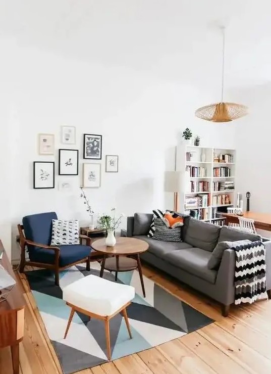 a mid-century modern living room with a bold printed rug, a grey sofa, a navy chair and a white stool, a cool gallery wall