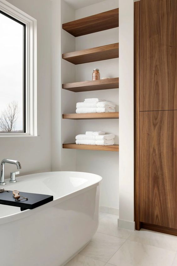 https://www.digsdigs.com/photos/2023/08/39-a-refined-contemporary-bathroom-clad-with-neutral-tiles-a-wardrobe-built-in-shelves-in-a-niche-an-oval-tub-and-a-window.jpg