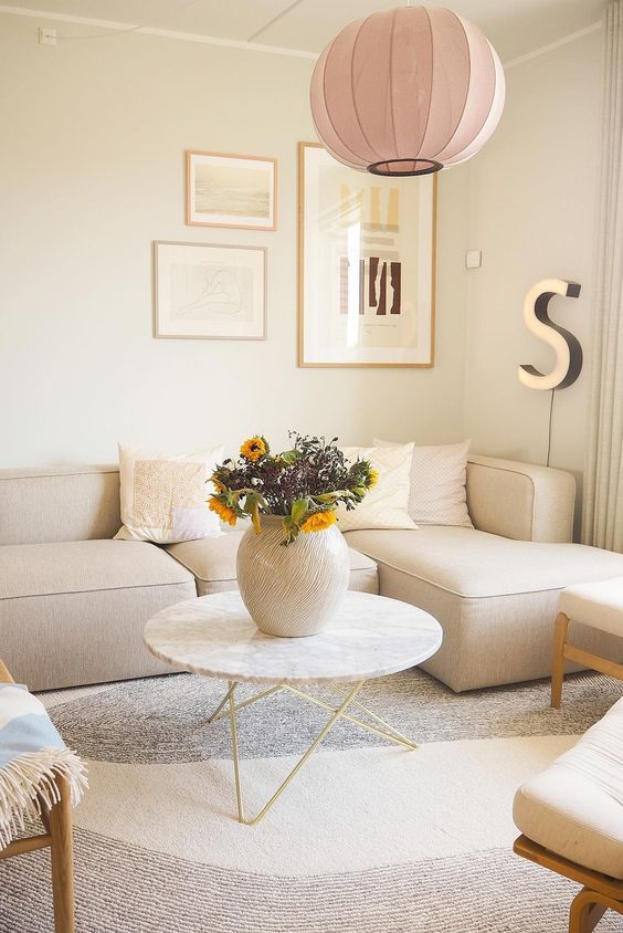 a neutral living room with a low olefin sofa, a coffee table, neutral chairs, a gallery wall and a pink pendant lamp