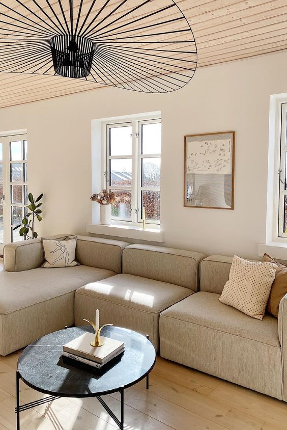 a stylish neutral living room with a grey olefin sofa and pillows, a black coffee table, a black pendant lamp and some art