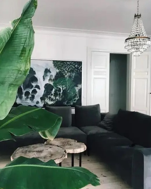 a beautiful eclectic living room with a black velvet sectional, a tree slice coffee table, a tropical print, a crystla chandelier and a statement plant