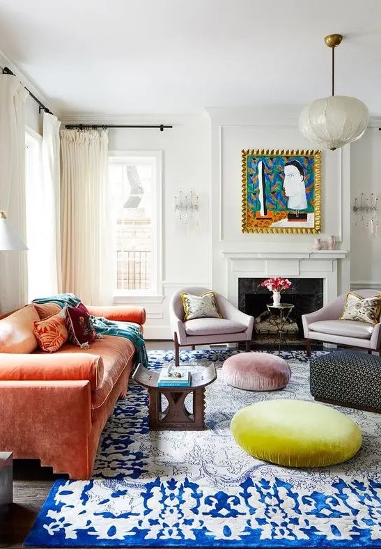 a colorful eclectic living room with a fireplace, lilac chairs, an orange velvet sofa, Moroccan furniture, a rug and poufs is bold