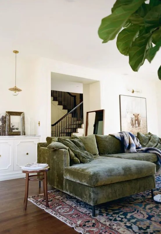 a farmhouse living room with a green velvet sectional, a boho printed rug, a white credenza with some decor and stained stools