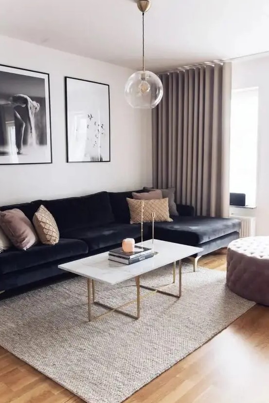 a refined living room with a black velvet sectional, a coffee table with gold legs, a tufted ottoman, a gallery wlal and greige curtains