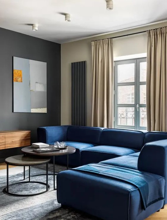 a minimalist living room with a black accent wall, a navy sofa, round tables, a floating credenza, neutral curtains and a pretty artwork