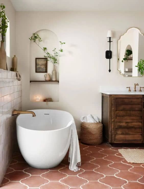 a Mediterranean farmhouse bathroom with a terracotta tile floor, a dark-stained vanity, an oval tub, niche shelves and some greenery