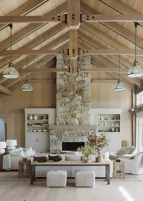 a barn living room with stained walls and a ceiling, with wooden beams, a fireplace clad with stone, neutral seating furniture and built-in storage units