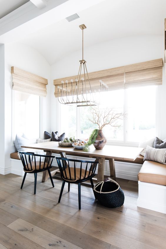 a beautiful and chic modern farmhouse dining room with a built-in corner bench, a stained table, black chairs, a chandelier and some pillows