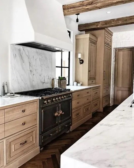 a beautiful and refined kitchen with light-stained cabinetry, a white hood and a white marble backsplash plus countertops