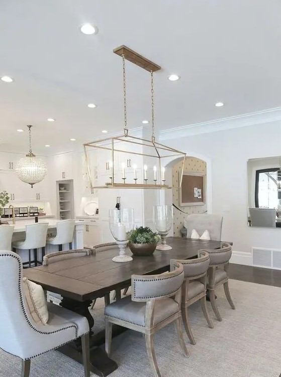 a beautiful neutral farmhouse dining room with a dark stained table, grey upholstered chairs, a lovely gilded pendant lamp and candles