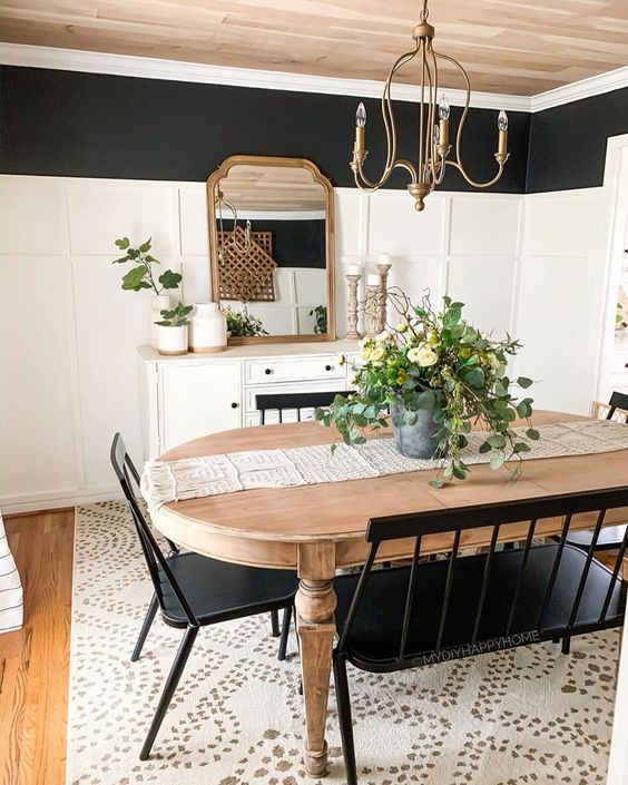 a black and white farmhouse dining room with a white sideboard, a stained vintage table, black chairs and a bench and a vintage chandelier