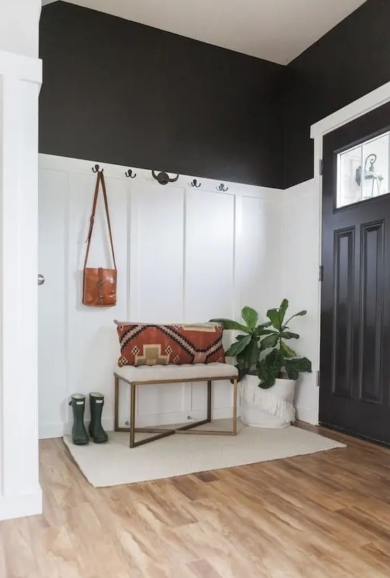 a black and white farmhouse entryway with paneling, a small bench with a pillow, a potted plant and a neutral rug