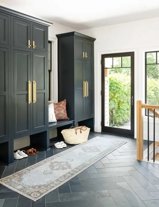 a black and white mudroom in farmhouse style, with large wardrobes, a built-in bench, a printed rug and a glass door