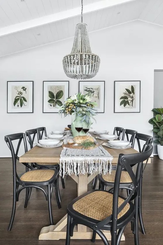 a chic modern country dining room with a stained table, black woven chairs, a wooden bead chandelier, a mini gallery wall