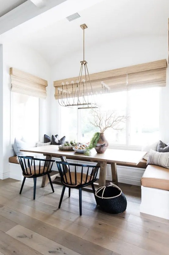 a chic modern country dining space with a built-in banquette seating, a stained table, black chairs and woven shades