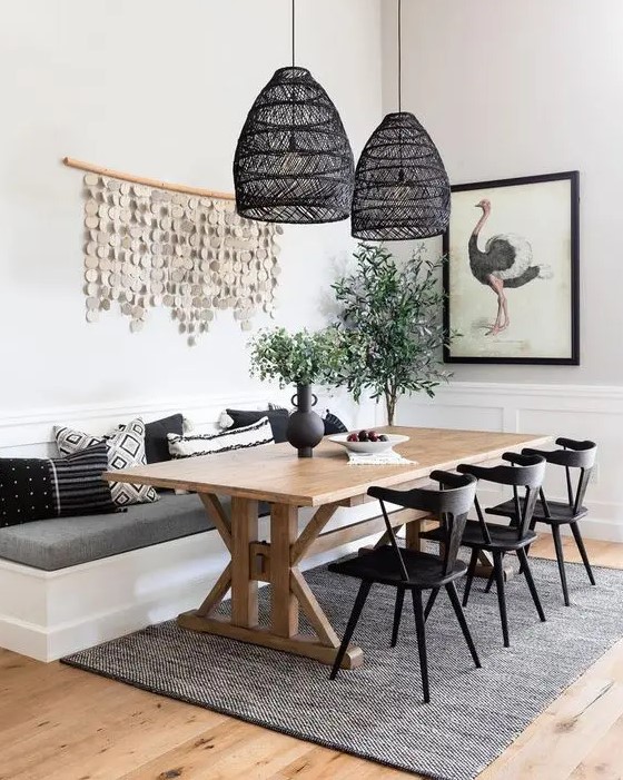 a chic modern farmhouse dining room with white paneled walls, a built-in banquette seating, a trestle dining table, black chairs and black woven pendant lamps