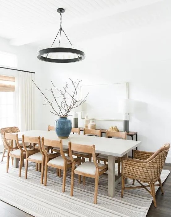 a chic modern farmhouse dining space with a large table, wooden and woven chairs, a metal chandelier and a console and lamps