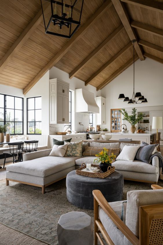 a chic modern farmhouse living room with a neutral sectional, a pouf, a chair, some chandeliers and greenery and blooms