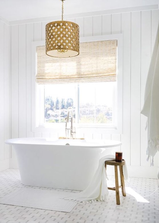 a chic white bathroom with shiplap walls, a mosaic tile floor, a tub by the window and a fabric covered vanity