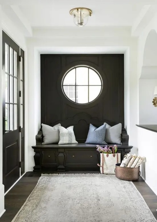 a cozy black and white mudroom with a black accent wall, a porthole window and a built-in bench, neutral pillows and a grey rug