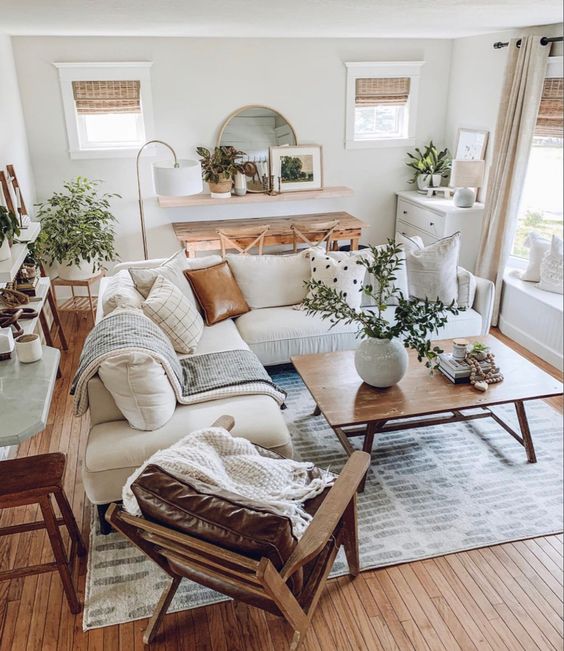 a cozy modern farmhouse living room with a console and chairs, a shelf with a mirror, a dresser, a white sectional, some tables and a leather chair